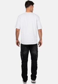 White short-sleeve t-shirt and black cargo pants with pockets. The pants feature a distressed texture and tapered fit. White sneakers complete the look.