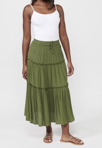 Falda larga verde con volantes y cintura de cordón, hecha de tela suave y texturizada, combinada con una camiseta sin mangas blanca y sandalias de tiras.