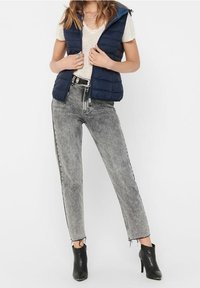 Marinblå puffermidja med huva över en ljus t-shirt, kombinerad med hög midja grå denimjeans och svarta anklarstövlar.