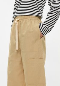 Μπεζ cargo παντελόνια με χαλαρή εφαρμογή, που διαθέτουν μεγάλες πλαϊνές τσέπες και ελαστική μέση με κορδόνι. Λείο, ελαφρύ ύφασμα.