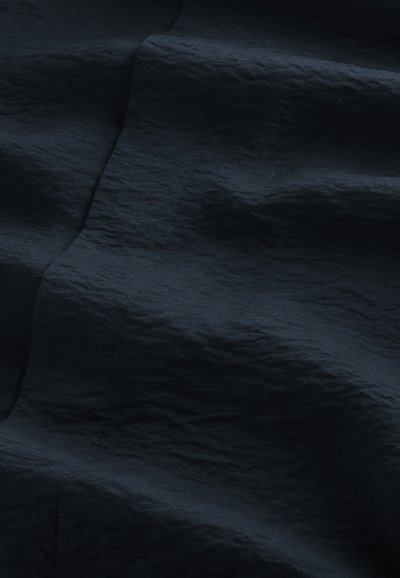 Tissu froissé bleu marine foncé avec une couture visible cousue verticalement sous un éclairage doux.