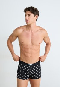 Boxer-briefs noirs avec un motif géométrique blanc, dotés d'une ceinture noire unie portant l'inscription "BOSS". Tissu doux avec un design ajusté.