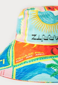 Pălărie de tip bucket colorată, realizată din material fabricat, având un amestec de nuanțe de albastru, roz și portocaliu cu modele tropicale și text, inclusiv „Praia de Pipa.”
