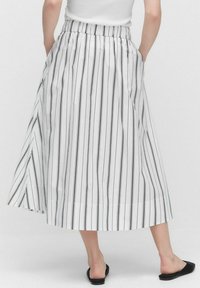 Jupe blanche avec des rayures verticales noires, taille élastique et poches latérales, présentant un design fluide et un ourlet légèrement asymétrique.