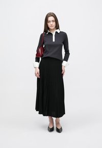 Μακριά μαύρη πλισέ φούστα, σε συνδυασμό με ένα σκουρόχρωμο πουλόβερ με λευκό γιακά. Αξεσουάρ περιλαμβάνουν μια μικρή κόκκινη τσάντα και μαύρα παπούτσια.