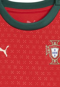Červený sportovní dres s texturovaným vzorem, zeleným límcem a bílým logem Puma. Obsahuje národní emblem Portugalska s jemným detailováním.