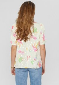 Blomsterblus i ljusbeige med rosa och gröna mönster, korta puffärmar, prickar och en ledig passform. Bakifrån visas en avslappnad design.