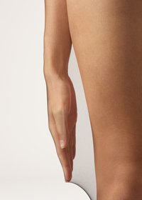 Nude, gennemsigtige strømpebukser med en glat, blød tekstur, der viser en hånd hvilende på et ben. Strømpebukserne er transparente og fremhæver hudtoner.