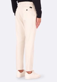 Pantaloni beige con una vestibilità rilassata, dotati di due tasche posteriori con chiusura a bottone, abbinati a sneakers bianche e a un maglione nero in maglia.