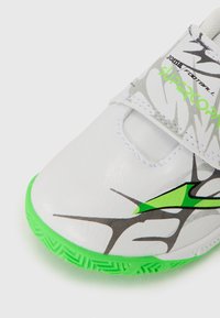Scarpa da calcio bianca con suola in gomma verde, parte superiore in sintetico texturizzato e motivi grafici grigi e neri. Presenta una fascia con chiusura a strappo.