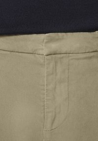 Beige bomullbyxor med en slät yta, som har en framficka och en snyggt sydd midja under en marinblå ribbad topp.