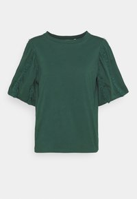 Blusa corta a maniche corte di colore verde scuro con maniche a sbuffo, caratterizzata da una rifinitura arricciata verticale e un colletto rotondo, su sfondo bianco.