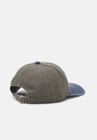 Szürke szövetsapka sötétkék karimával, állítható pánttal és kerek kék gombbal a tetején. Texturált felület és hat szellőzőnyílás.