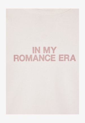 T-shirt in cotone rosa chiaro con scritte in rilievo di un rosa più scuro che recitano "NELLA MIA ERA ROMANTICA." Design semplice con scollo rotondo.