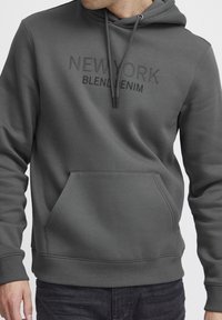 Gray sweatshirt with a hood, featuring an embossed "NEW YORK" and "BLEND DENIM" text. Kangaroo pocket and ribbed cuffs and hem detail.