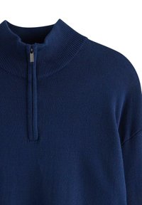 Granatowy sweter z wysokim kołnierzem i półzamkiem. Wykonany z miękkiego materiału dzianinowego, z prążkowaną strukturą na kołnierzu i mankietach.