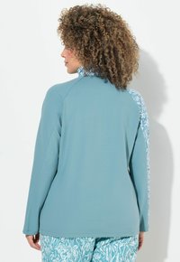 Maglietta a maniche lunghe di colore azzurro chiaro con un accento decorativo sulla spalla. Il tessuto appare liscio con una vestibilità comoda.