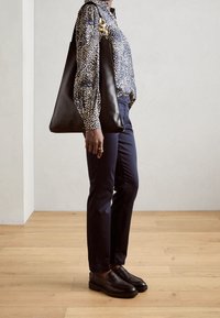 Sac en cuir noir en toile lisse, quincaillerie dorée, chemise à motifs pois, pantalon bleu marine et mocassins noirs au design épuré.