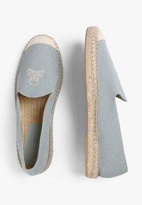 Lichtblauwe canvas espadrilles met een beige canvas bies, voorzien van een doodskop en gekruiste botten logo, en een jute touwtextuur op de zool.