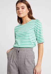 Grøn- og hvidstribet kortærmet t-shirt lavet af blødt stof, parret med højtaljede gråternet bukser med folder og sidelommer.