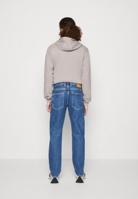 Sudadera gris recortada con cordón, combinada con jeans azules de pierna recta y bolsillos traseros. Diseño limpio con un acabado minimalista.