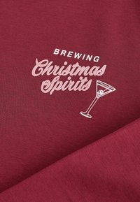 Burgundijas audums ar baltu uzrakstu "Ziemassvētku dziru vārīšana" un martini glāzes grafiku, gluda tekstūra ar ikdienišķu dizainu.