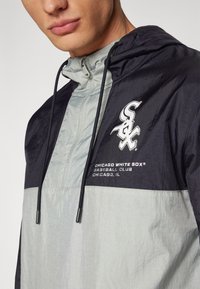 Lightweight hooded windbreaker in gray and black with drawstrings, featuring "Chicago White Sox" logo and text on the chest area.