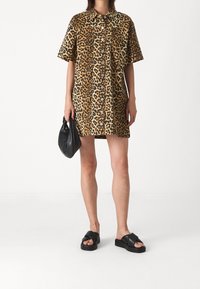 Paidatunika, jossa on leopardi-kuosi, lyhyet hihat, nappisuljenta ja kontrastiset ruskeat ja beige sävyt. Yhdistetty mustan käsilaukun ja sandaalien kanssa.