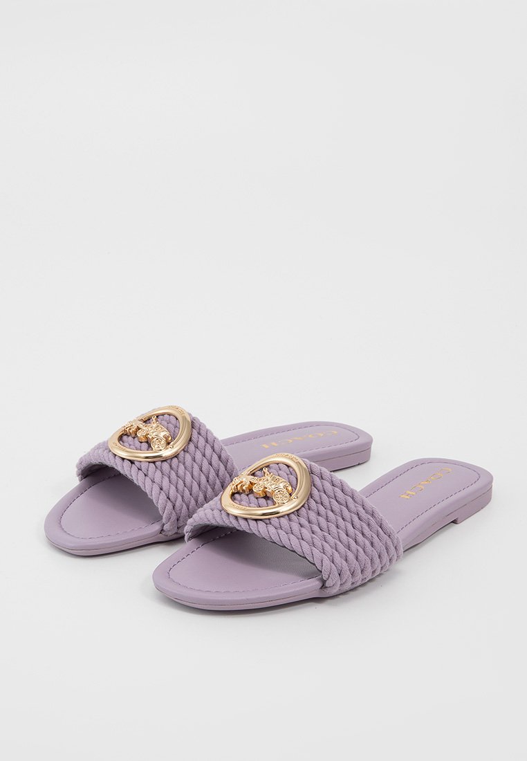 Białe płaskie sandały z lnu z plecionymi tekstylnymi paskami, z złotymi klamrami w kształcie serca oraz gładką gumową podeszwą.