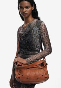 Braune Leder-Schultertasche mit strukturiertem Finish, dekorativen Nähten und metallischen Nieten. Enthält einen langen Tragegurt.