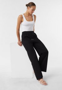 Black wide-leg pants with a drawstring waistband, paired with a fitted white tank top. The outfit features minimalistic design and smooth textures.