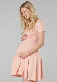 Hellrosa Umstands-Kurzarmkleid mit tailliertem Oberteil und schwingendem Rock, aus weichem, elastischem Material gefertigt. Glatte Textur und knielang.