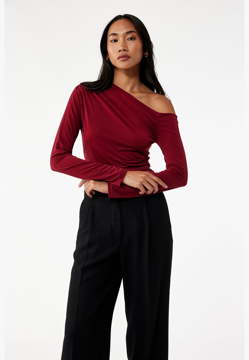 Bordeaux langærmet top med off-shoulder design og gathered tekstur, parret med højhentede sorte bukser.