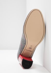 Chaussure à talon haut à carreaux avec un motif écossais gris, talon rouge brillant et semelle beige lisse, affichant le logo de la marque et la taille 37.
