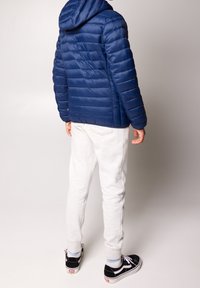 Navy puffer jacket with a hood, quilted texture and elastic cuffs, paired with light grey joggers and black Vans sneakers.