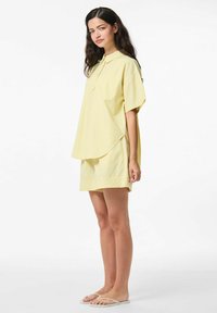 Dzeltena svītraina īsā piedurkne krekls ar apkakli un kabatu, apvienots ar atbilstošām šortiem. Audums šķiet viegls un gluds.