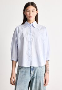 Ανοιχτό μπλε, ελαφρύ πουκάμισο με κουμπιά μπροστά, γιακά και μανίκια τριών τετάρτων. Ομαλή υφή και άνετη εφαρμογή.