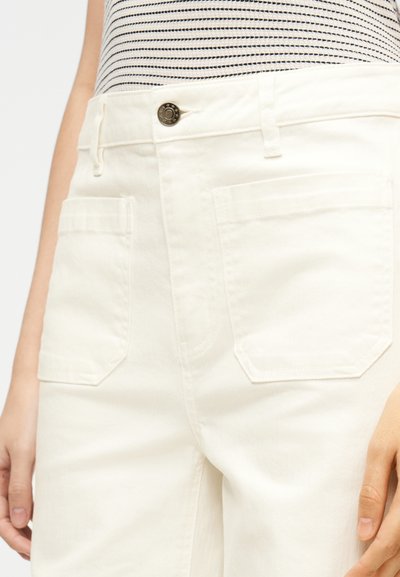Pantalon en denim blanc taille haute avec une fermeture à boutons sur le devant, deux grandes poches arrière, et une texture lisse. Tissu rayé visible à la taille.