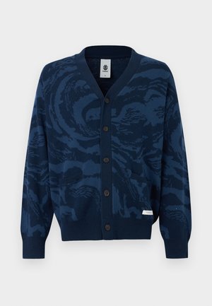 Tumši zils pogājams kardigans ar abstraktu tumšāka zila rakstu, ribotiem aproču un apakšmalas malām, divām priekšpusē kabatām un nelielu auduma zīmola etiķeti.