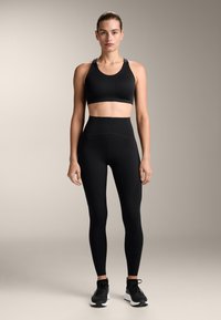 Svart sport-bh med breda axelremmar och höga leggings med textured sömmar och en åtsittande design, parat med svarta träningsskor.