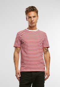 Sarkans un balts svītrots T-krekls ar apaļu kakla izgriezumu, īsām piedurknēm un pieguļošu piegriezumu, savienots ar melnām biksēm.