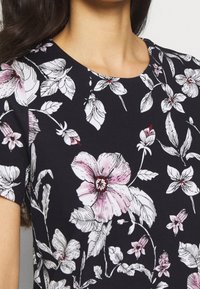 Halenka s květinovým potiskem na černém pozadí, krátké rukávy, kulatý výstřih a růžové a bílé květinové vzory s podrobnými listy.