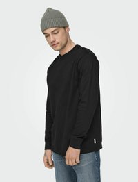 Schwarz-langärmliges Shirt aus Baumwollstoff mit Rundhalsausschnitt und gerippten Bündchen, kombiniert mit einer gerippten grauen Mütze.