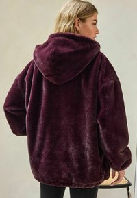 Ylihuokoinen burgundinpunainen fleecehuppari pehmeällä tekstuurilla, suurella hupulla ja alaslasketuilla hartioilla, jossa on rento istuvuus ja resorit hihansuissa.