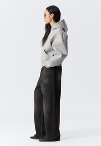 Grå huvtröja med huva, sidofickor, kombinerad med löst sittande svarta jeans som har subtila texturränder och raka ben.