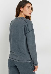 Grå långärmad sweatshirt i mjukt tyg, med en avslappnad passform, synliga sömmar och rundad halsringning; bärs med matchande byxor.