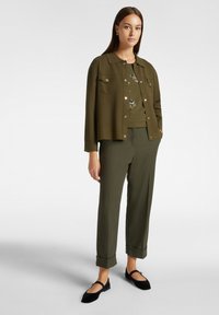 Completo verde oliva composto da giacca con colletto e tasche frontali, abbinato a pantaloni tapered coordinati, completato da ballerine nere.