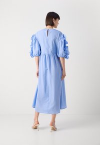 Lyseblå midi-kjole med puffede flæser på ærmerne, nøglehul detalje i ryggen og glat tekstur, parret med beige strop sandaler.