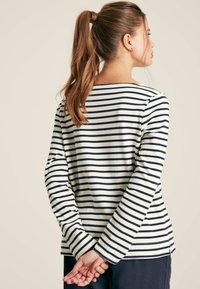 Gestreiftes Langarmshirt in Weiß und Marineblau, mit einem Bootsausschnitt, lockerer Passform und seitlichen Schlitzen am Saum für mehr Bewegungsfreiheit.