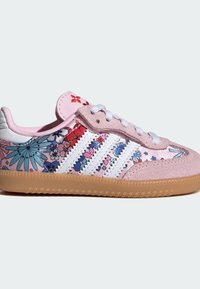 Zapatillas deportivas rosas con patrones florales en azul, morado y rojo. Rayas blancas a los lados, textura de ante y suela de goma color caramelo.